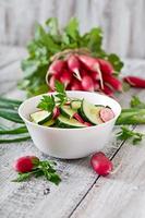 Fresh salad of cucumbers and radishes in a white bowl on the old wooden background photo