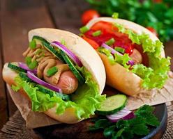 Hot Dog con salsa de tomate, mostaza, lechuga y verduras en la mesa de madera foto