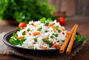 Appetizing healthy rice with vegetables in white plate on a wooden background.