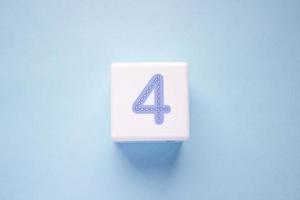 Close-up photo of a white plastic cube with a blue number 4 on a blue background. Object in the center of the photo