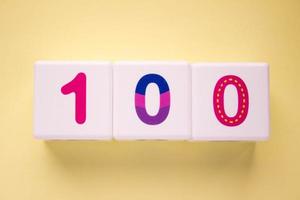 Close-up photo of a white plastic cubes with a colorful number 100 on a yellow background. Object in the center of the photo