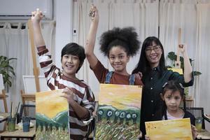 Group of art people in classroom studio, a teacher and student kids proud show painting work, an acrylic color picture on canvas, creative learning with talents skill at elementary school education. photo