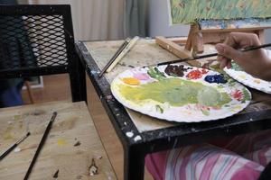 Close-up shot, acrylic colors palette, mixing and painting a picture by artist's hand, vivid multicolor in canvas with easel, colorful creativity with talent skills, artistic imagination design. photo
