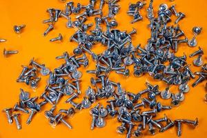 Many metal self-tapping screws made of steel in a glass, in bucket jar. self-tapping screw for metal, for iron, chrome-plated self-tapping screw, on an orange yellow background, photo