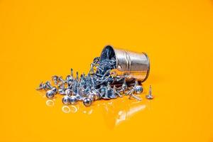 Many metal self-tapping screws made of steel in a glass, in bucket jar. self-tapping screw for metal, for iron, chrome-plated self-tapping screw, on an orange yellow background, photo