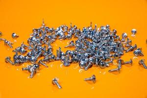 Many metal self-tapping screws made of steel in a glass, in bucket jar. self-tapping screw for metal, for iron, chrome-plated self-tapping screw, on an orange yellow background, photo