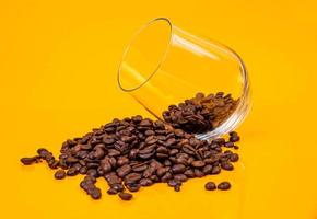 Dropped Many roasted coffee beans in a glass, in bucket jar. self-tapping screw for metal, for iron, chrome-plated self-tapping screw, orange yellow background photo