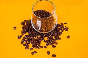 Dropped Many roasted coffee beans in a glass, in bucket jar. self-tapping screw for metal, for iron, chrome-plated self-tapping screw, orange yellow background photo