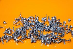 Many metal self-tapping screws made of steel in a glass, in bucket jar. self-tapping screw for metal, for iron, chrome-plated self-tapping screw, on an orange yellow background, photo