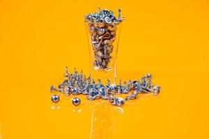 Many metal self-tapping screws made of steel in a glass, in bucket jar. self-tapping screw for metal, for iron, chrome-plated self-tapping screw, on an orange yellow background, photo