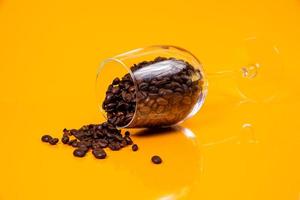 Dropped Many roasted coffee beans in a glass, in bucket jar. self-tapping screw for metal, for iron, chrome-plated self-tapping screw, orange yellow background photo