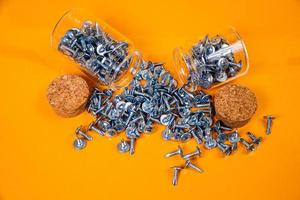 Many metal self-tapping screws made of steel in a glass, in bucket jar. self-tapping screw for metal, for iron, chrome-plated self-tapping screw, on an orange yellow background, photo