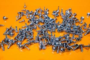 Many metal self-tapping screws made of steel in a glass, in bucket jar. self-tapping screw for metal, for iron, chrome-plated self-tapping screw, on an orange yellow background, photo