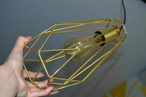 yellow lamp with broken lines in the steampunk style in female hands with manicure. unusual pear-shaped lamp to maintain light and heat in the room. the lamp inside makes yellow photo