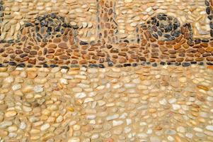 The texture of the stone wall, the road from small round and oval stones with abstract lines laid out patterns of sandy seams of natural old yellow black brown. The background photo