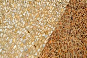 The texture of the stone wall, the road from small round and oval stones with abstract lines laid out patterns with two-color sandy seams of natural old yellow black brown. The background photo