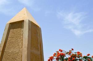 un gran obelisco puntiagudo hecho de piedra amarilla en egipto contra un cielo azul y flores rojas foto