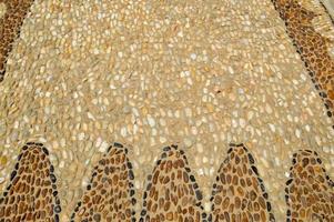 The texture of the stone wall, the road from small round and oval stones with abstract lines laid out patterns of sandy seams of natural old yellow black brown. The background photo