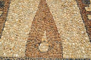 la textura de la pared de piedra, el camino de pequeñas piedras redondas y ovaladas con líneas abstractas dispuestas patrones de costuras arenosas de marrón amarillo negro antiguo natural. el fondo foto