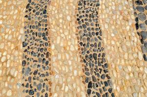 The texture of the stone wall, the road from small round and oval stones with abstract lines laid out patterns of sandy seams of natural old yellow black brown. The background photo