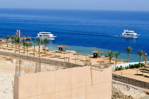 construcción de un hotel en el desierto en un cálido centro vacacional exótico del sur tropical frente a un mar azul de palmeras y barcos blancos foto