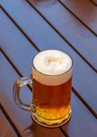 Mug of beer with white dense foam on a wooden background.