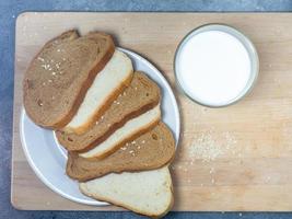 trozos de centeno y pan blanco con un vaso de leche en una tabla de cocina. desayuno saludable. productos de panadería con semillas de sésamo. foto