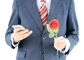 Businessman in suit holding smartphone and red rose photo