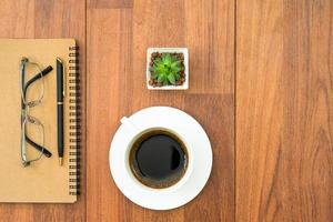 anteojos y libreta con taza de café en cubierta de madera foto