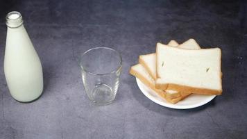 assiette de pain blanc tranché et personne verse du lait dans un verre