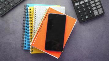 Smartphone on a pile of spiral notebooks, a calculator, top view video