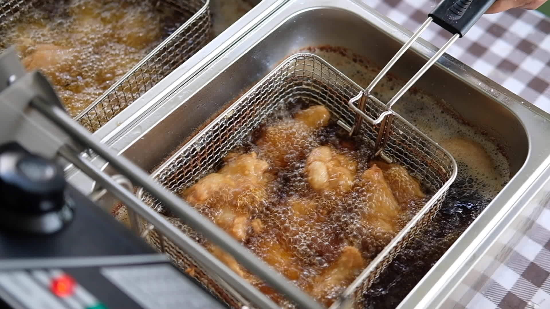 Frying chicken in deep fryer with bubbles of the oil are boiling while