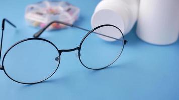 Round framed glasses and pill bottles on blue background video