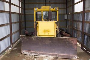 Large wheeled tractor with a dozer blade for clearing roads from snow. Yellow wheel loader in the garage. photo