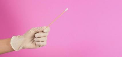 un bastón de algodón para la prueba de hisopo en la mano del dedo con guantes médicos blancos sobre fondo rosa. de cerca. foto