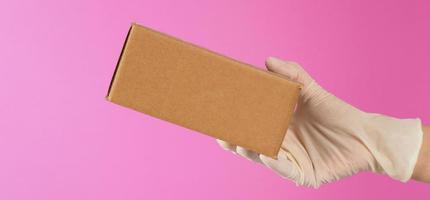 The hand is holding a brown box isolated on pink background. photo