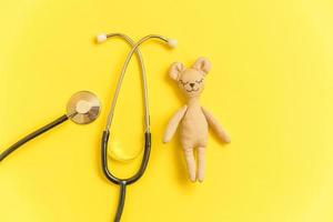 Simply minimal design toy bear and medicine equipment stethoscope isolated on yellow background. Health care children doctor concept. Pediatrician symbol. Flat lay top view layout, copy space photo