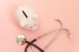 Medicine doctor equipment stethoscope and piggy bank isolated on pink pastel background. Health care financial checkup or saving for medical insurance costs concept. Flat lay top view copy space. photo