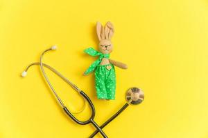 Simply minimal design toy bunny and medicine equipment stethoscope isolated on yellow background. Health care children doctor concept. Pediatrician symbol. Flat lay top view layout, copy space photo