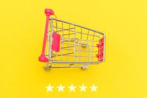 Small supermarket grocery push cart for shopping toy with wheels and 5 stars rating isolated on yellow background. Retail consumer buying online assessment and review concept. photo