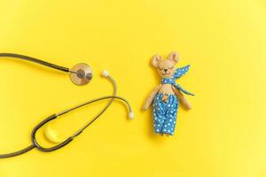 Simply minimal design toy bear and medicine equipment stethoscope isolated on yellow background. Health care children doctor concept. Pediatrician symbol. Flat lay top view layout, copy space photo