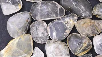 Rutilated quartz heap jewel stones texture on black stone background. Moving right seamless loop backdrop. video