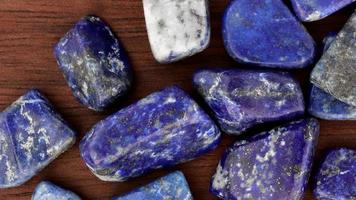 lapis lazuli mucchio su gioiello pietre struttura su Marrone verniciato legna sfondo. in movimento giusto senza soluzione di continuità ciclo continuo sfondo. video