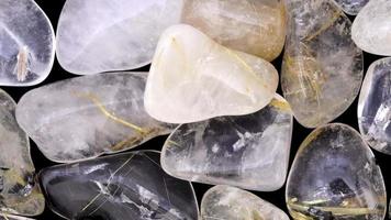 Rutilated quartz heap jewel stones texture on black background. Moving right seamless loop backdrop. video