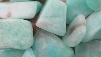 Amazonite jewel heap on light wood texture. Pile mineral pebbles background. Moving right seamless loop backdrop. video