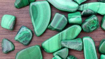 Malachite heap up jewel stones texture on brown varnished wood background. Moving right seamless loop backdrop. video
