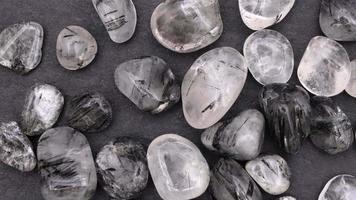 Tourmalinated quartz heap up jewel stones texture on black stone background. Moving right seamless loop backdrop. video