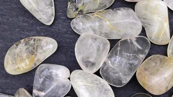 Rutilated quartz heap up jewel stones texture on black stone background. Moving right seamless loop backdrop. video