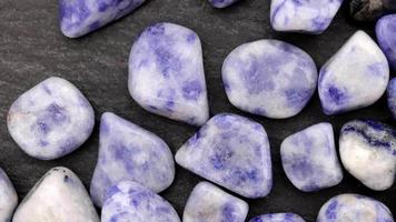 sodalite mucchio su gioiello pietre struttura su nero pietra sfondo. in movimento giusto senza soluzione di continuità ciclo continuo sfondo. video