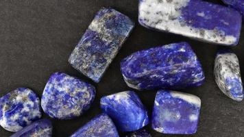 Lapis lazuli heap up jewel stones texture on black stone background. Moving right seamless loop backdrop. video